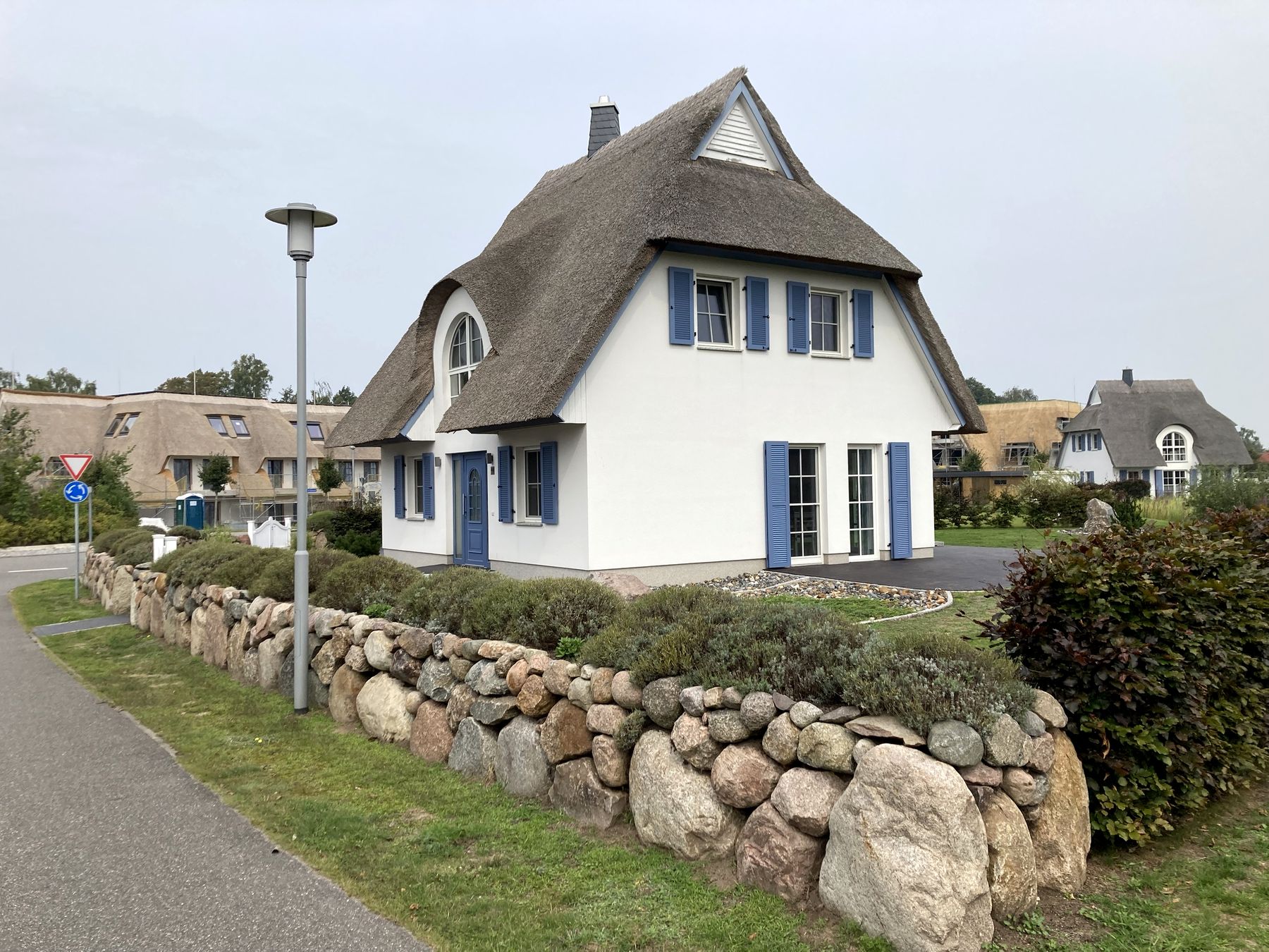 Reetdachhaus mit blauen Fensterläden hinter einer Feldsteinmauer in Fuhlendorf